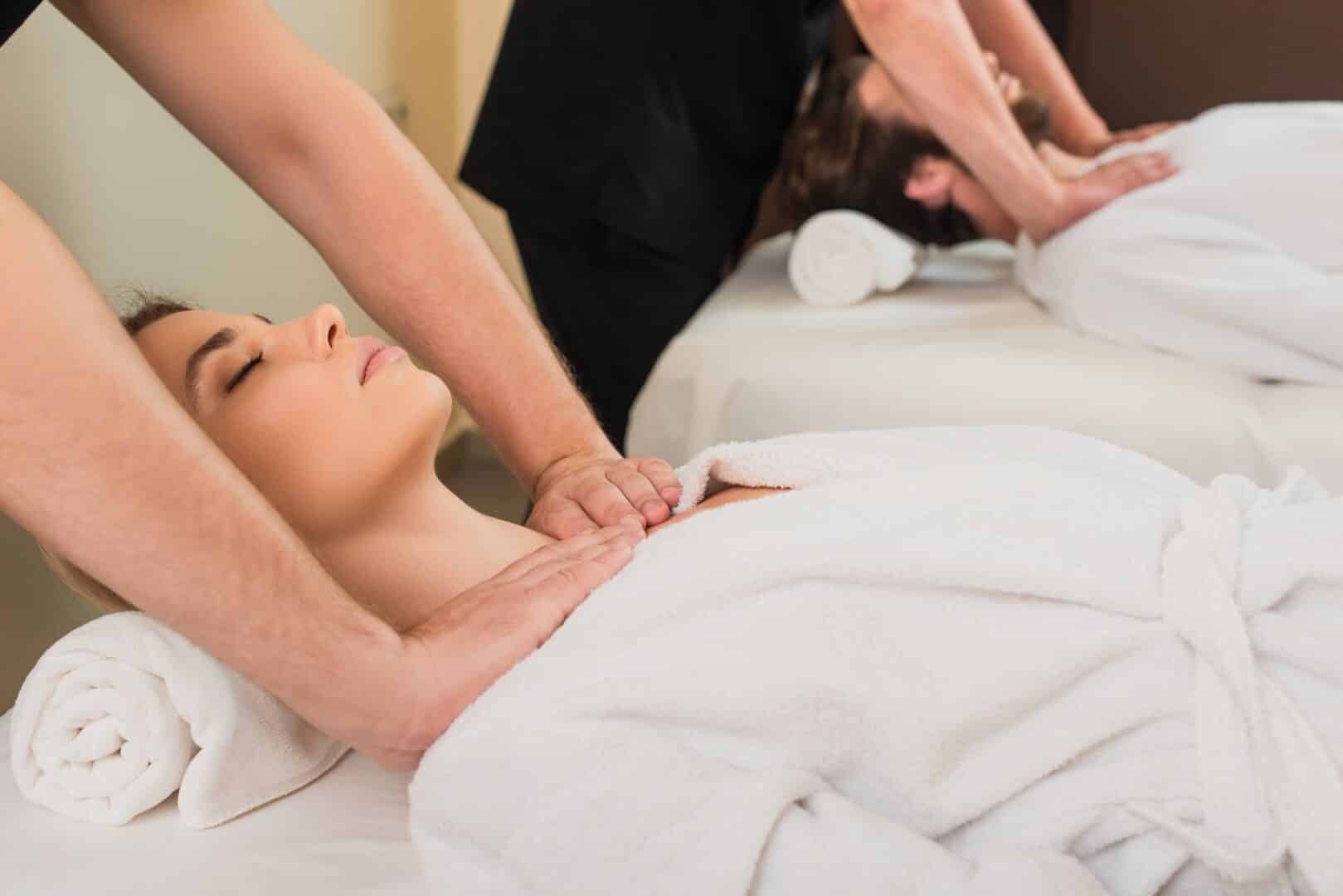 masseur doing shoulders massage to woman in bathrobe near colleague and man in spa center